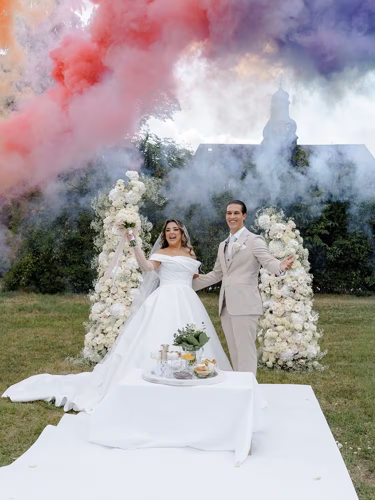 Hochzeitspaar vor einem Blumenbogen mit farbigem Rauch